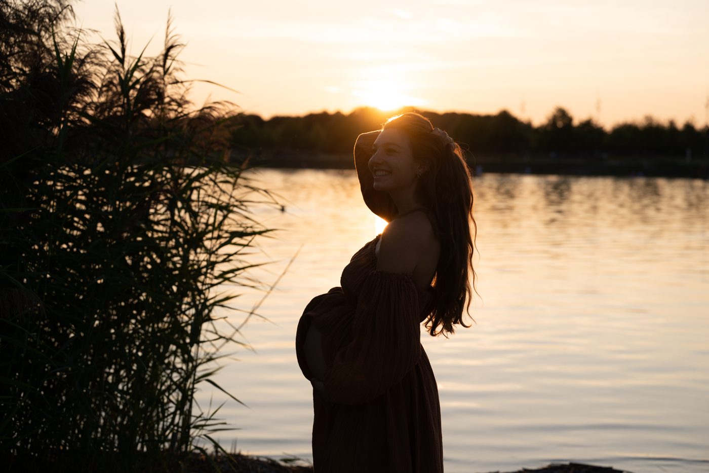 Schwangere Frau am See bei Sonnenuntergang